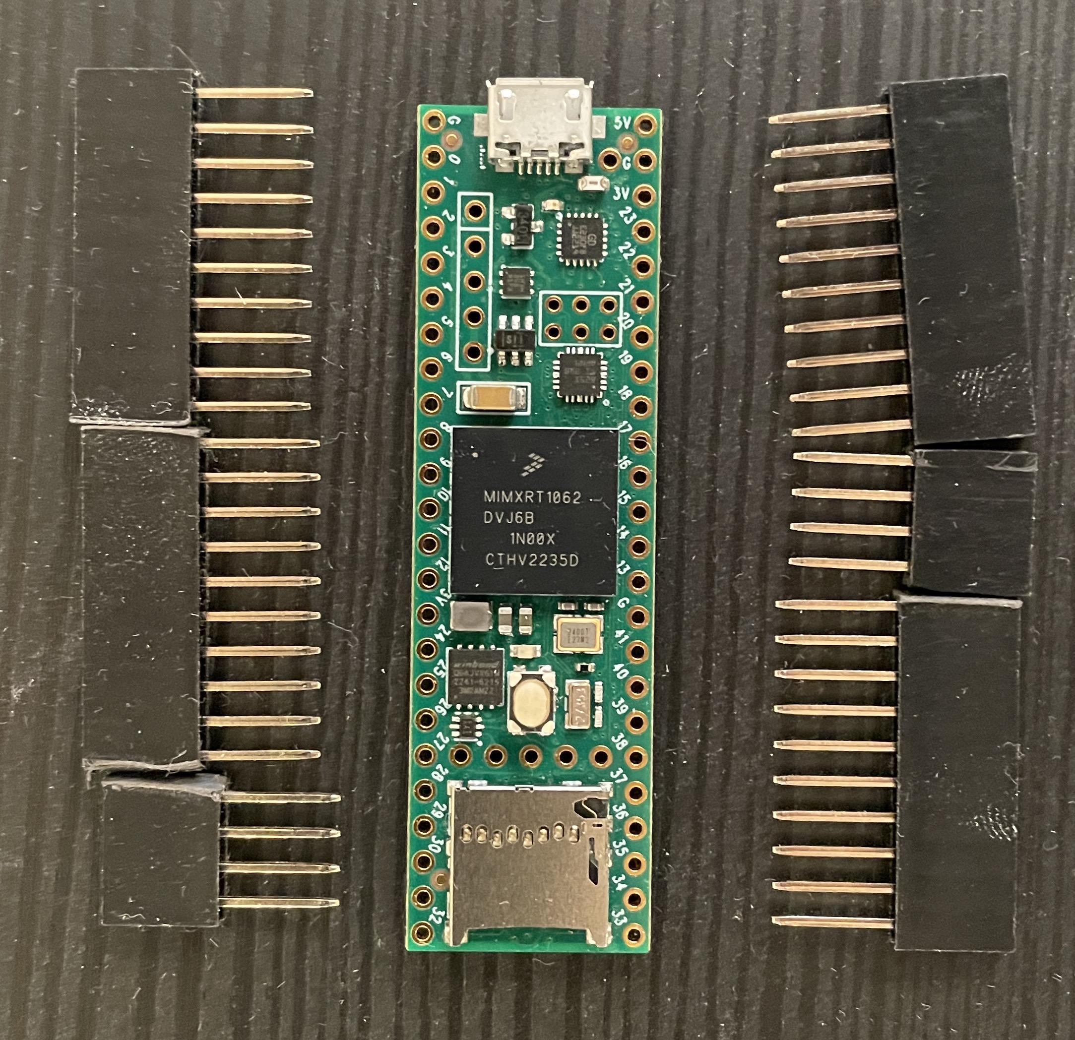 The Teensy 4.1 board with unsoldered stacking female header pins lying next to it on a table showing that the pins are longer than standard hearders